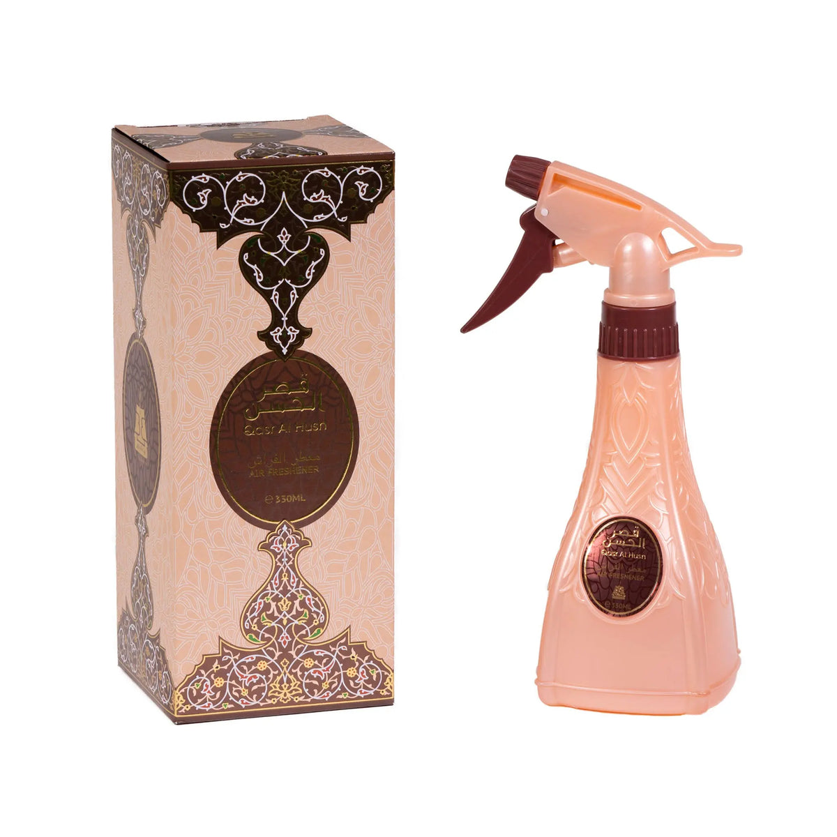 The image shows two items: on the left, a rectangular box with intricate patterns in shades of beige, brown, and gold, featuring Arabic calligraphy and English text that reads "Qasr Al Husn Air Freshener," with a capacity of "350ML." On the right, there's a spray bottle with a peach-colored body and a dark brown spray head. The bottle has a similar design as the box with a label that includes Arabic calligraphy and the same English text, "Qasr Al Husn." 