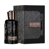 A sleek black and gray box of "Ajayeb Dubai" Eau de Parfum by Lattafa, featuring a textured design and the product name in white and bronze text on the front. The box is placed next to a matching perfume bottle with a glossy, hammered black finish.