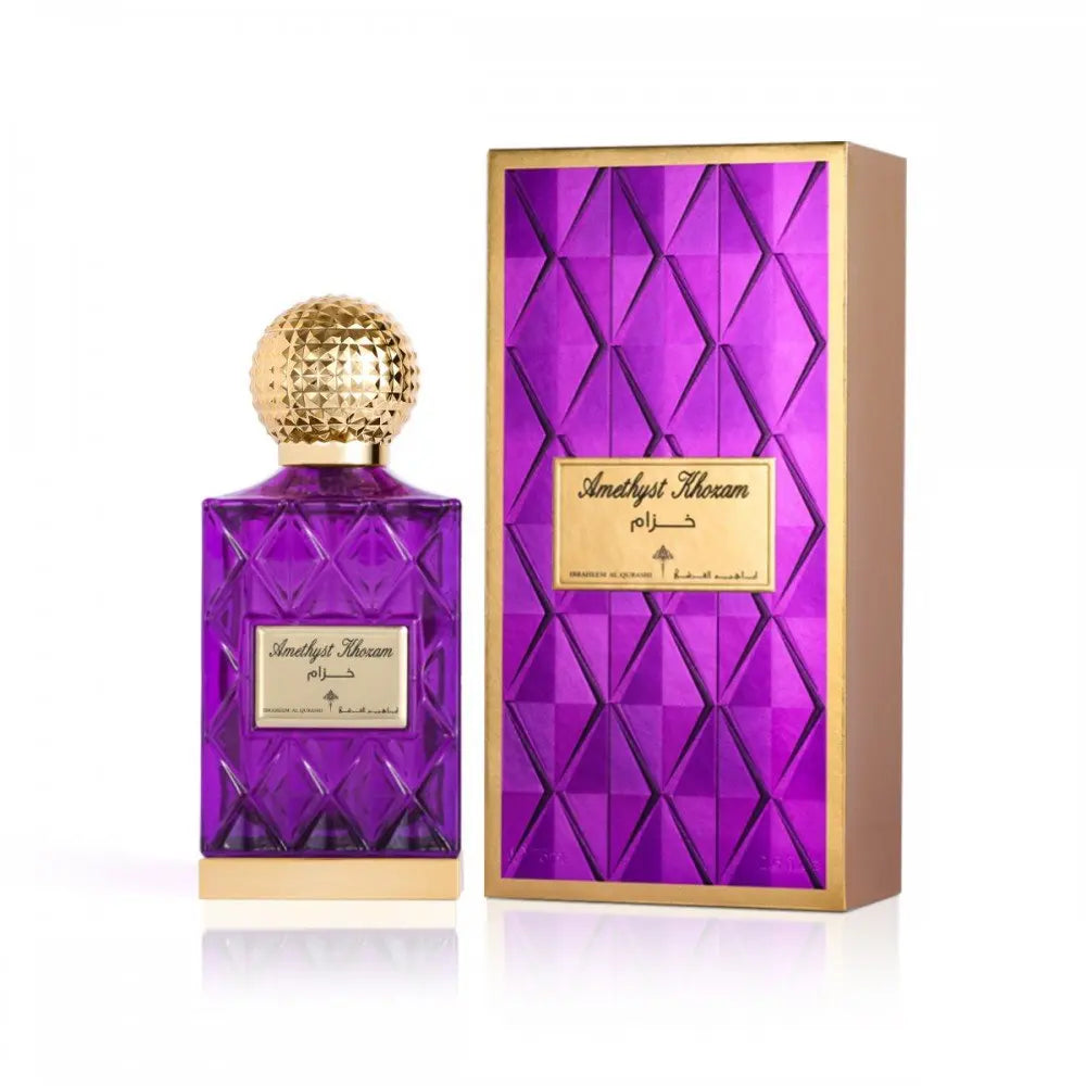 The image features a luxurious purple glass perfume bottle with a golden, textured cap next to its packaging. The bottle has a label with "Amethyst Khozam" written in both Arabic and English, signifying the fragrance's name from the brand Ibraheem Al Qurashi. The design of the bottle has a faceted pattern, giving it a jewel-like appearance. The packaging box is gold with a purple faceted design, complementing the bottle's design, and has a label that matches the one on the bottle.