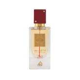 Image of a rectangular clear glass perfume bottle with a red cap embellished with two crystals. The bottle features a gold label with intricate arabesque designs and Arabic calligraphy that reads '??? ????' (Ana Abiyedh), with 'ROUGE' printed in red below. Below the gold label is the brand logo in gold with a flame-like design and the word 'Lattafa'. The perfume liquid appears to be a pale amber color, and the overall design suggests luxury and exotic allure.