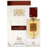 Image featuring a clear glass perfume bottle with a gold label and red cap, in front of its white and brown packaging box. The bottle's gold label has arabesque designs and Arabic calligraphy reading '??? ????' (Ana Abiyedh) and 'ROUGE' in red, with a red line that continues down from the label. The cap is adorned with two crystals. The box has a similar design, with the brand name 'Lattafa' and 'Eau de Parfum' written in brown, along with 'Natural Spray - Vaporisateur'.