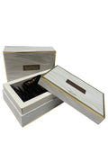 The image features an elegant product packaging for "Bakhoor Asmara". It consists of two rectangular boxes with a wood grain design and golden accents. The larger box is open, revealing a collection of dark-colored incense chips inside. Both boxes have Arabic script and English text on them. The design is sophisticated, with the combination of wood texture print and gold creating a sense of luxury.