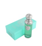 The image shows a perfume bottle named "Capri" from the Gissah collection, placed next to its packaging. The perfume bottle is cylindrical with a teal glass body and a decorative silver cap featuring intricate embossed patterns. A silver medallion with an ornate design is affixed to the front of the bottle. The packaging is a matching teal box with a mandala-like design and the names "Gissah" and "Capri" printed on it.