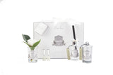 A luxury gift set from Côte Noire featuring a variety of products. Included are a clear glass vase with an artificial white rose and green leaves, two small glass bottles labeled 'Gardenia Blanc,' a reed diffuser in a clear glass container with black reeds, and a clear glass candle with a lid. All items have an ornate silver label and are presented in front of a white gift box with silver accents and a label that reads 'Côte Noire Luxury Gift Set.