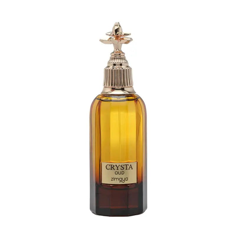 The image shows a bottle of "CRYSTA OUD" by Zimaya, a luxury fragrance. The bottle is tall with a rectangular base and rounded shoulders, filled with a rich amber-colored liquid. It features a thick, dark brown base that lightens as it reaches the top. The cap is a distinctive spray nozzle with a textured ring and an ornate, gold-toned decorative element on top that looks like a stylized flower. 