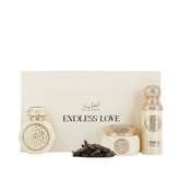 The image shows two perfume bottles from Gissah's "Endless Love" collection, displayed in front of a cream-colored box that has the collection's name printed on it. One bottle is short and wide with a flat cap, while the other is tall and cylindrical with a rounded cap. Both bottles are an off-white color and feature ornate gold medallions. Next to the bottles are a cluster of dark-colored items that resemble cloves, which might indicate the scent profile of the perfumes.