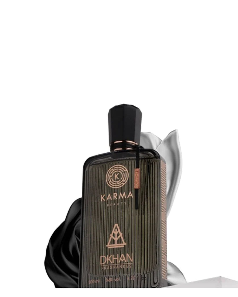 This image showcases a dark, elegantly textured perfume bottle for "Karma Beauty" by DKHAN Fragrances. The bottle appears to be made of ribbed glass with a luxurious matte finish and features the Karma Beauty logo embossed in a circular design at the top. Below the logo is the distinctive DKHAN Fragrances logo, resembling a heart within a diamond shape, set above the product details which indicate a 100ml quantity and 80% vol. The cap is a sleek black with a copper band.