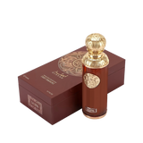 The image features "La Luna" by Gissah, displayed alongside its packaging. The perfume bottle is a sleek copper color with a gold ornate medallion and an intricately designed gold spherical cap. The packaging is a deep brown box with a textured surface and a large gold circular mandala design on the top. The box also has the name "Gissah" and "LA LUNA" along with the description "SIGNATURE COLLECTION LIGHT FRAGRANCE."