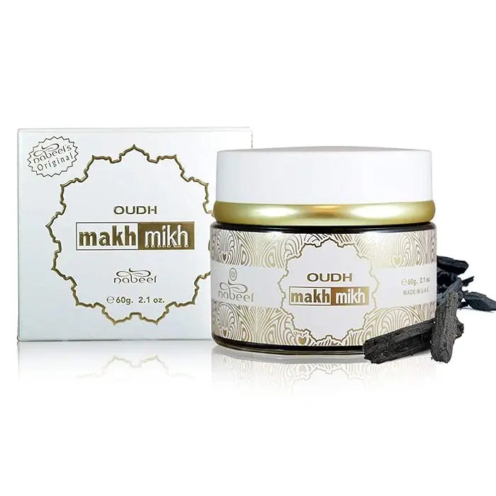 The image shows a container of "OUDH makh mikh" by Nabeel Perfumes. The container is a short, wide jar with a white body and a golden lid, sitting next to its packaging box. The jar is labeled with decorative, intricate gold and white patterns, and the product name is displayed prominently in the center. The box mirrors the jar's design with a similar pattern and color scheme, featuring a central label with the product name and the brand's logo in a stylized font.