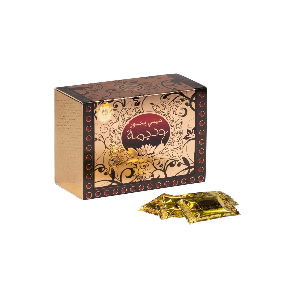 The image features a box for "Mini Wadeema Bakhoor" from Nabeel Perfumes. The box has a dark brown background with elaborate golden floral patterns and a central maroon label with Arabic script and the product name in English. The left side of the box is gold with embossed Arabic script. In front of the box lie several small, sealed golden packets with what appears to be the same name and branding as the box.