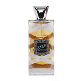 The image displays a perfume bottle with the following attributes:  The bottle is rectangular with a clear glass design, allowing a view of the amber-colored perfume inside. A silver ribbon with the words "Oud Mood" printed in a repeating pattern wraps around the bottle. The central label is ornate with a black background and white decorative border; it features Arabic calligraphy and the word "Reminiscence" in English script.