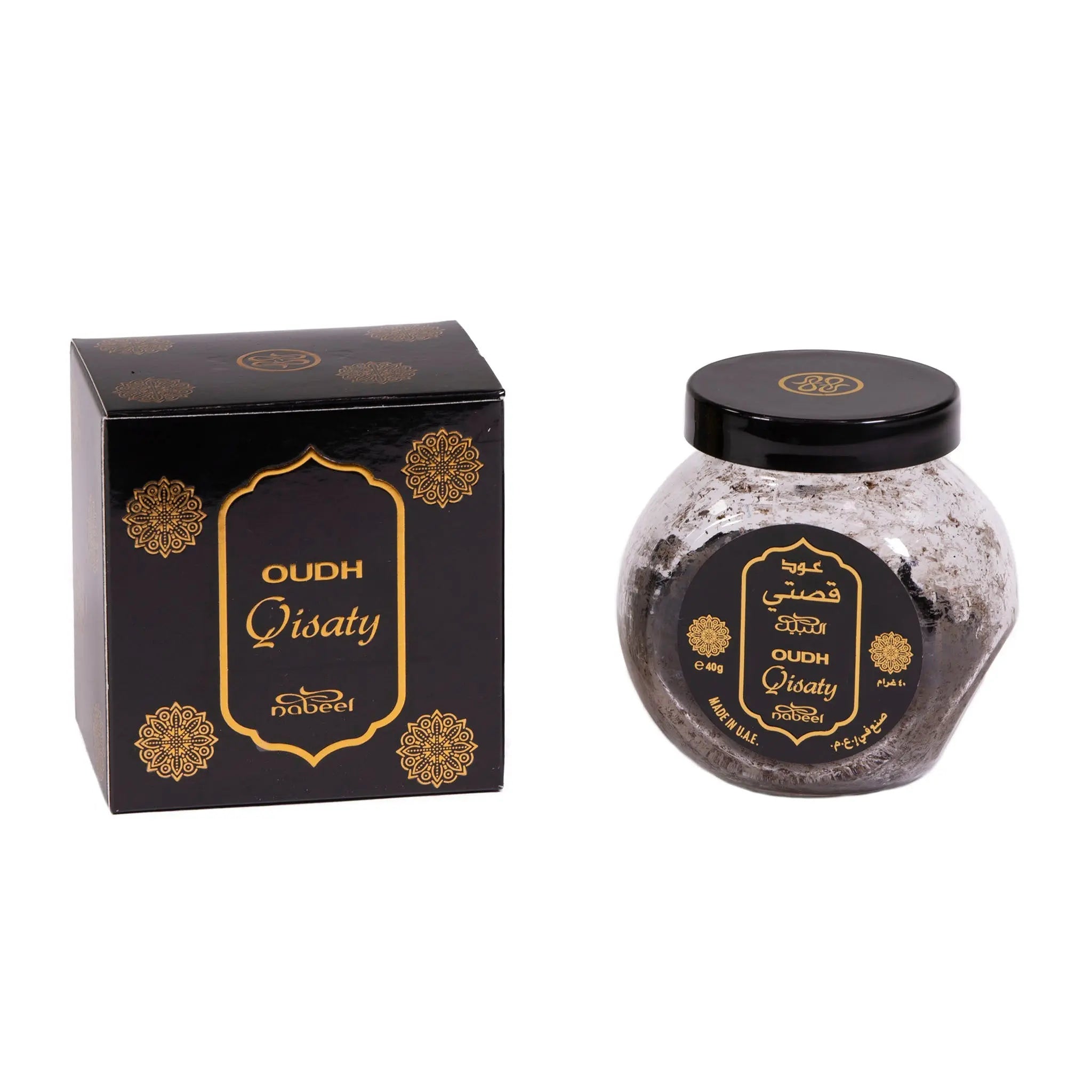 The image presents "OUDH Qistaty" by Nabeel, featuring a luxurious black box and a transparent glass jar with a black lid. Both items are adorned with elegant gold floral patterns and labels that include the product name in Arabic and English. The jar's label indicates the weight as "e 40g". The design of the packaging conveys an opulent and traditional aesthetic, with the black and gold color scheme adding a touch of sophistication.