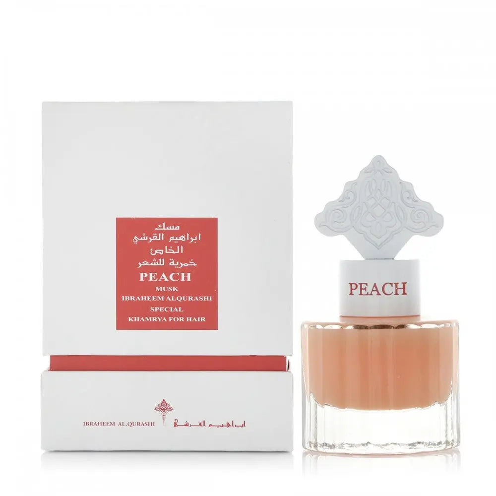 The image shows a fragrance product consisting of a square-shaped bottle and a matching box. The bottle is transparent with a peach-colored liquid and has a white cap with the word "PEACH" in matching peach color. It also features an ornate white cap design with an intricate pattern. The white box has a red label with gold and white text that reads "PEACH MUSK IBRAHEEM AL.QURASHI SPECIAL KHAMRIYA FOR HAIR"