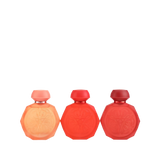 A set of three Gissah perfume bottles in a range of red hues, each with an octagonal shape and intricate embossed designs on the front. The bottles feature smooth, matching caps and come in shades of peach, vibrant red, and deep red. The elegant and minimalist design highlights the gradient of colors, making the set visually appealing and sophisticated.