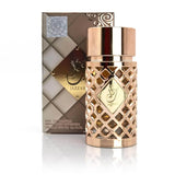  The image shows a rose gold perfume bottle of "Jazzab Gold" by Ard Al Zaafaran. This cylindrical bottle features a lattice design with diamond-shaped cutouts and a reflective surface cap. In the foreground, the bottle displays a gold label with "Jazzab" in Arabic calligraphy. The background includes the perfume's matching box, which has a textured white and brown design with the same label as the bottle, indicating the fragrance's name.  The packaging's design elements suggest elegance and luxury.