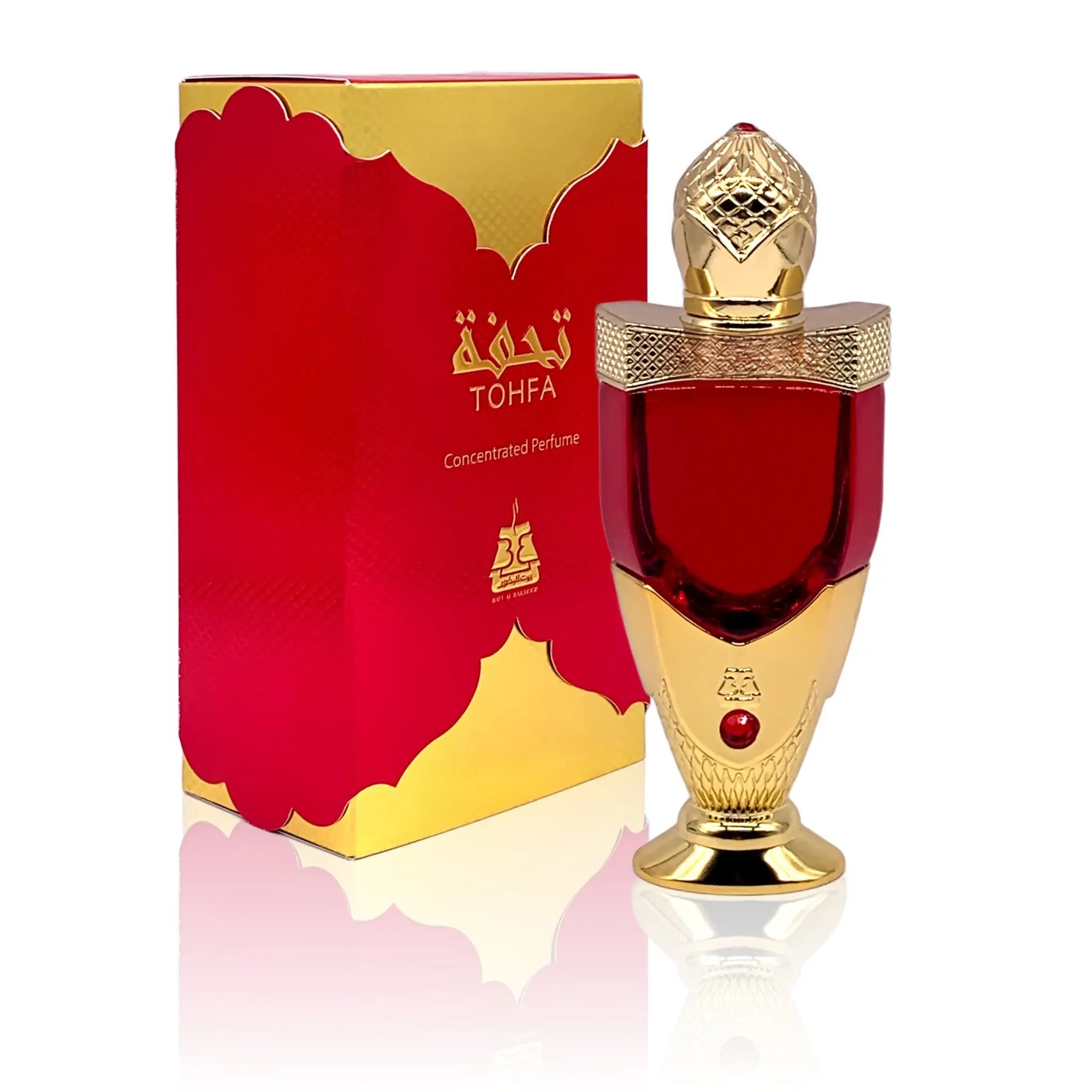 The image shows a luxurious perfume bottle next to its packaging. The bottle has a rich red color with a golden cap, detailed with intricate patterns and topped with a clear faceted finial that resembles a gem. The base and neck of the bottle also feature golden accents. A red gem is embedded in the golden section of the bottle. The packaging box is red with a golden border and carries the brand name "TOHFA" in gold lettering.