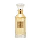The image is of a perfume bottle:  The bottle has a rectangular shape with clear glass, revealing the golden-colored liquid perfume inside. It features a gold-colored neck and a white, bristle-like applicator that resembles a traditional shaving brush. The front of the bottle has a simple, elegant label with "VELVET OUD" in black letters and Arabic script below it.