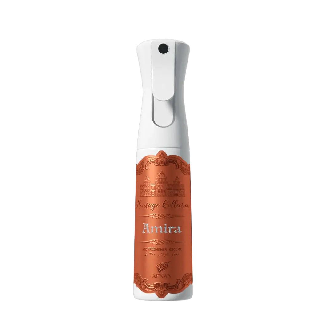 The image displays a spray bottle designed for air freshener, with the upper half in white and the lower half wrapped in a coppery maroon label. The label features ornate detailing and the text "Heritage Collection" at the top, with "Amira" written prominently in the center. The logo "AFNAN" is also present towards the bottom of the label. The bottle has a white spray nozzle and trigger. The background is a soft, neutral shade, which complements the product's colors.