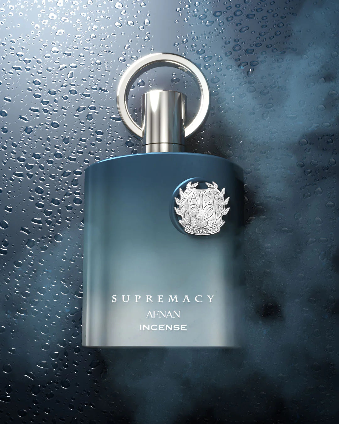 The image displays a luxurious perfume bottle set against a dark, moody background with water droplets, suggesting a fresh or aquatic theme. The bottle has a gradient of navy blue at the bottom, fading into a clear glass towards the top. It is adorned with a silver emblem featuring intricate designs.  The overall image conveys a sense of high-end sophistication and the essence of the fragrance within.