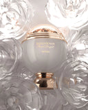 The image shows a perfume bottle with a clean and elegant design. The bottle has a spherical white body with a golden band that reads "SOUVENIR Floral Bouquet AFNAN." Above the band is a clear dome, encasing what appears to be a cluster of golden petals or flakes, giving a sense of luxury. The bottle rests on a golden pedestal base that complements the golden accents.