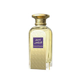 The image features a perfume bottle with a luxurious golden hue. The design has a rectangular form with rounded shoulders leading to a short neck and a textured gold cap that resembles twisted rope. The main body of the bottle is adorned with a textured pattern, giving it an embossed look. A purple rectangular label with Arabic calligraphy is centered on the bottle, and below it, in smaller English lettering, is "Naseej Al Khuzama." 
