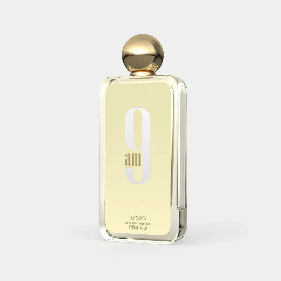 The image shows a rectangular perfume bottle with a gold cap and a clear glass body. It features a prominent "9 am" in stylized font on the front, with the word "AFNAN" written beneath it in smaller, capitalized font. The label indicates that it is an "eau de parfum vaporisateur" and the size is "100ml, 3.4fl.oz." The background is a plain, light color providing a neutral backdrop that accentuates the perfume bottle.