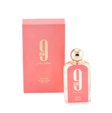 The image displays a rectangular glass perfume bottle and its corresponding box. The bottle is clear with a pink hue and has a white oval label with a large "9" and "am" in black font, with "pour femme" in smaller script below it. The cap is a polished gold sphere. At the bottom of the bottle, "AFNAN" is printed, along with "100ml | 3.4fl.oz". The box is a matching pink color with the same "9 am pour femme" branding and additional text "eau de parfum vaporisateur". 