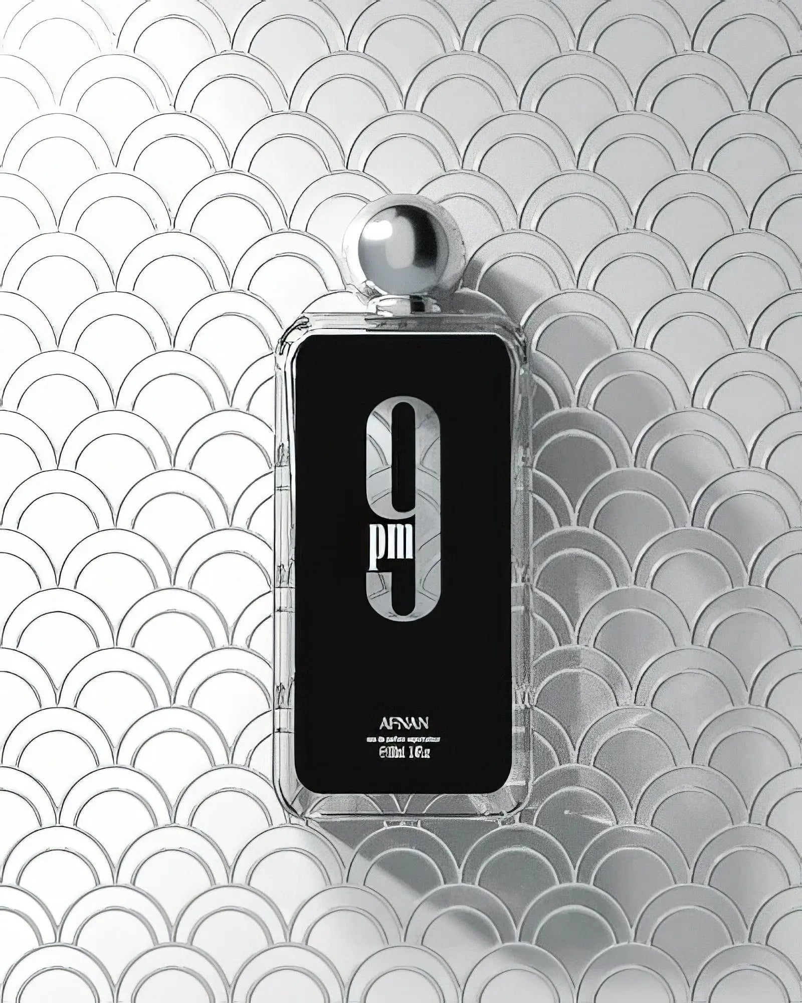 Afnan 9 PM perfume bottle displayed against a textured silver scallop-patterned backdrop, emphasizing the fragrance's sleek design and modern aesthetics.