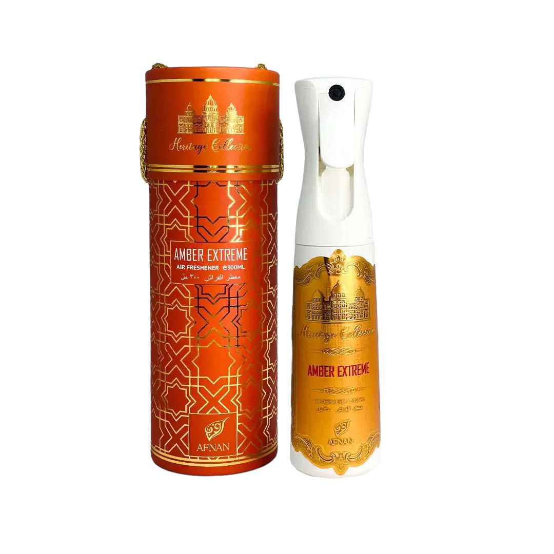 The image shows an air freshener product with its cylindrical packaging. The packaging is orange with intricate gold geometric patterns and includes a depiction of palatial architecture, the words "Heritage Collection," and "AMBER EXTREME" in bold letters. Below, the brand name "AFNAN" is visible. 