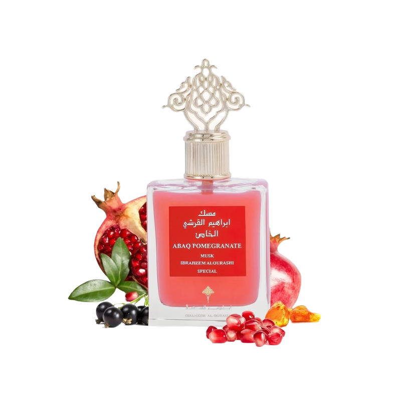 The image shows a product, which is a bottle of perfume named "ABAQ POMEGRANATE MUSK" by Ibraheem Al Qurashi. The perfume bottle has a clear, ornate design with a gold-colored cap featuring intricate patterns. The liquid inside the bottle is a rich red color, and the label is red with white and gold text. Surrounding the bottle are several pomegranates and loose pomegranate seeds, as well as a few black currants, which are likely meant to suggest the fragrance notes of the perfume. 
