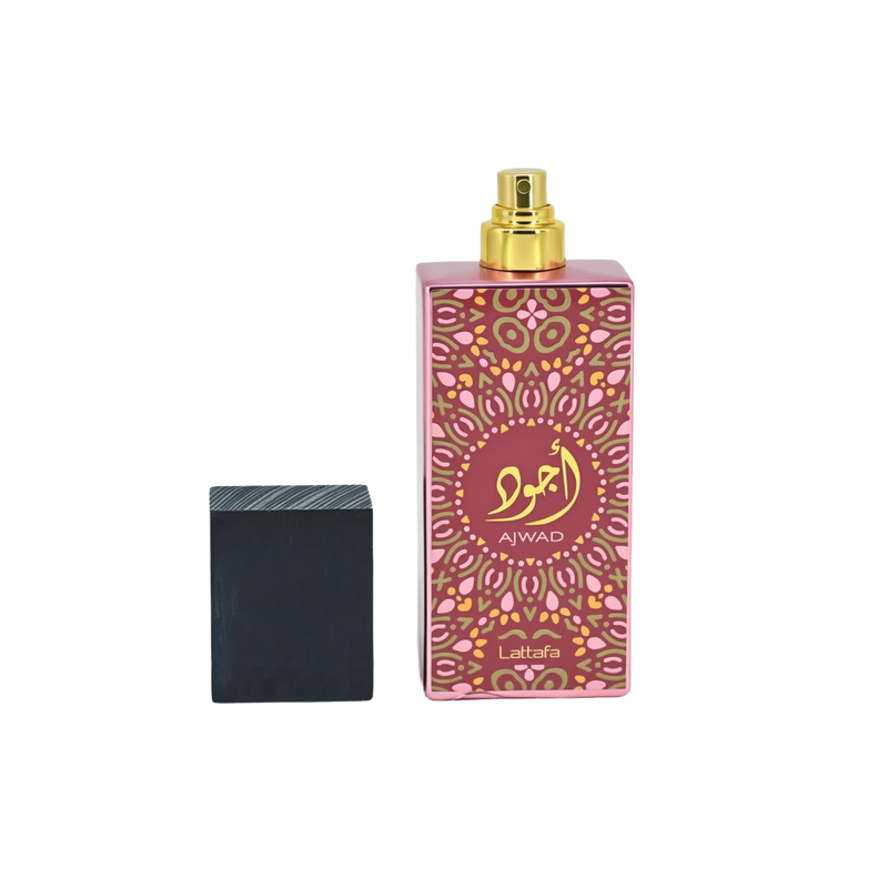Image of a tall pink perfume bottle with a gold spray nozzle, placed upright next to its black textured cap which is lying on its side. The bottle has a decorative pattern in a lighter pink hue with a central circular label containing gold Arabic calligraphy and the word 'AJWAD'. Below the pattern, 'Lattafa' is written in small gold letters. The bottle is reflected on a glossy surface below, indicating a polished presentation.