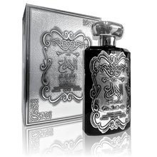 The image displays a product set consisting of a perfume bottle and its packaging box. Both the bottle and the box are adorned with elaborate embossed silver designs. The central motif is a stylized, ornate emblem with what appears to be Arabic script at the center, possibly the brand or fragrance name, 'AL IBDA'.  The box has a textured surface with the same motif repeated in a more subdued pattern in the background. 