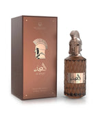 A product shot showing Le Falcone Niche Collection’s “Al Majd” perfume against a white background: on the left, a tall matte-brown rectangular gift box with a glossy copper front panel featuring the Le Falcone logo, a stylized profile of a warrior’s helmet, Arabic calligraphy, and the words “Al Majd” (Extrait de Parfum, 85?ml / 2.8?fl?oz). On the right sits the matching perfume bottle — an amber, diamond-cut glass cylinder topped by a sculpted bronze wlarrior-helmet cap.