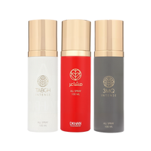 This image displays a trio of All Over Spray bottles from DKHAN Fragrances, each containing 100 ml of product. From left to right: the first bottle is white with a gold cap and the 'TABGH INTENSE' label in a clear font; the middle bottle is vibrant red with a gold cap and labeled 'club INTENSE' in white lettering; the third bottle is a dark grey with a gold cap and the '3MQ INTENSE' label. Each bottle features the DKHAN Fragrances logo—a stylized heart within a diamond shape—above the label.