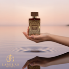 Hand holding Zimaya Amber Is Great perfume bottle above calm water.