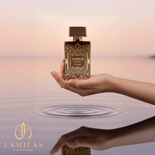 Hand holding Zimaya Amber Is Great perfume bottle above calm water.