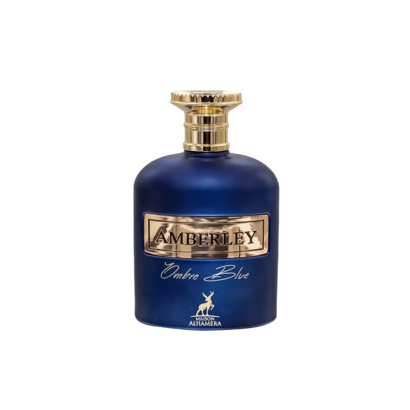 The bottle is a deep cobalt blue with a smooth, rounded shape. It has a metallic gold label with the name "AMBERLEY" embossed in the center. Below the main label, in elegant script, is the name "Ombre Blue." A small, gold stag emblem is placed at the bottom center of the bottle, indicating the logo for "MAISON ALHAMBRA." The cap of the bottle is gold with a textured design, resembling a crown or cog. 