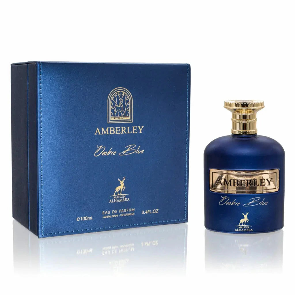 The image features a set of perfume products, including a bottle and its packaging:  To the right is a cobalt blue perfume bottle similar to the previously described one, with a gold label reading "AMBERLEY" above "Ombre Blue" in cursive script, and a small gold stag logo below. The bottle has a gold cap with a ribbed texture. Both the bottle and the box are presented against a reflective white surface with a subtle shadow, indicating a reflective and bright background. 