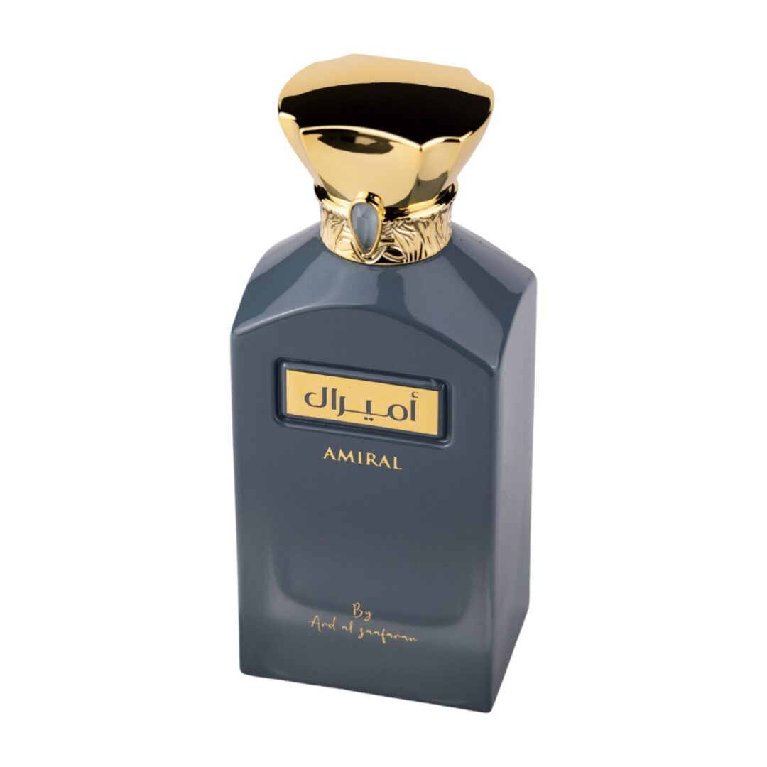 The image shows a bottle of "AMIRAL" by Ard Al Zaafaran perfume. The bottle is a sleek matte grey with a luxurious gold cap designed to resemble a regal crown, adorned with a gold ring and a gemstone at the neck. The front of the bottle features the name "AMIRAL" in black on a gold label, with Arabic script above it. Below the label, there is a signature that says "By Ard Al Zaafaran".