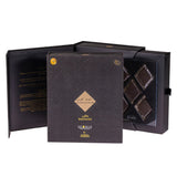 The image showcases an open luxury gift box set containing Arabian musk bakhoor. The box is a deep black color with golden accents. The inner left side features text, presumably describing the contents or giving instructions for use in both Arabic and English. The right side has a neatly arranged stack of dark, square bakhoor blocks, possibly made of compressed scented wood or resin.