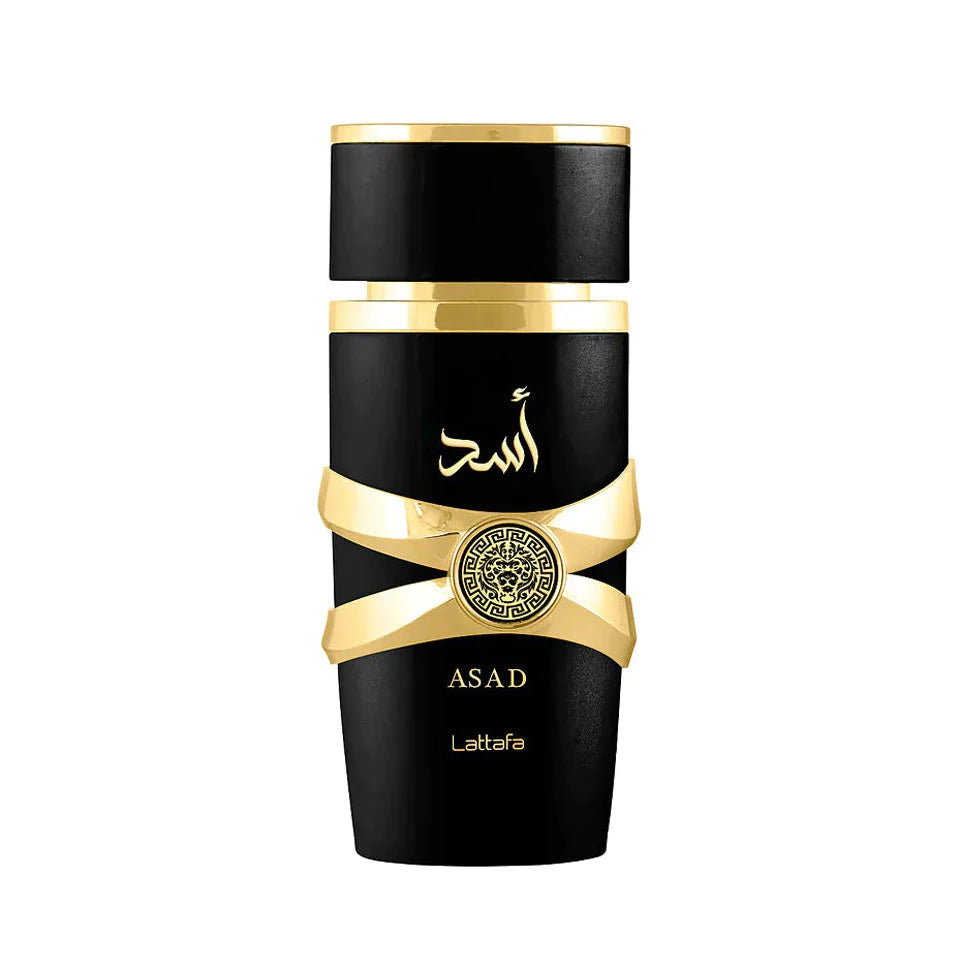 This image shows a sleek, cylindrical perfume bottle named "ASAD" by Lattafa. The bottle is glossy black with a matte black cap. A distinctive gold ribbon-like band wraps around the bottle, holding a circular gold emblem with intricate designs. Below the band, the name "ASAD" is written in gold along with the Lattafa brand name. Arabic calligraphy in gold is featured above the gold band, likely spelling the same name "ASAD."