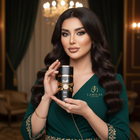 Elegant woman in a green gown holds the black and gold Lattafa Asad perfume bottle.