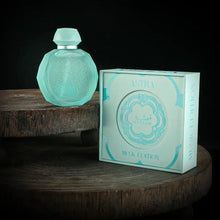 A pastel blue octagonal perfume bottle with intricate embossed designs on the front, displayed on a wooden surface against a dark background. The bottle features a matching pastel blue cap and a silver collar. Next to the bottle is its elegant pastel blue box, labeled "Astra Musk Edition" with the Gissah brand name prominently featured. 