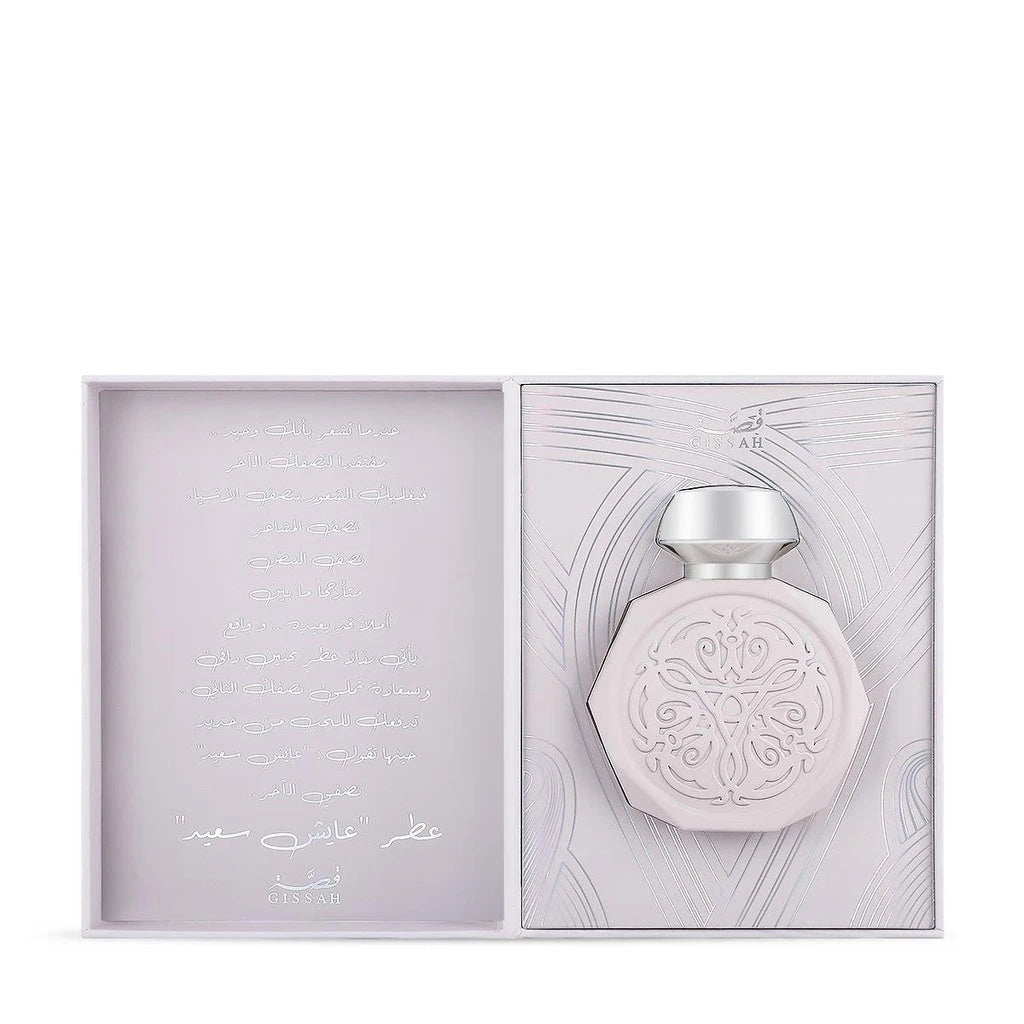 A pale pink, octagonal perfume bottle with intricate, embossed designs on the front, displayed inside an open box. The box features elegant, subtle patterns and the Gissah brand name. The left side of the box contains text in Arabic script, adding a luxurious and personalized touch. The bottle has a sleek, metallic silver cap that complements its delicate design.