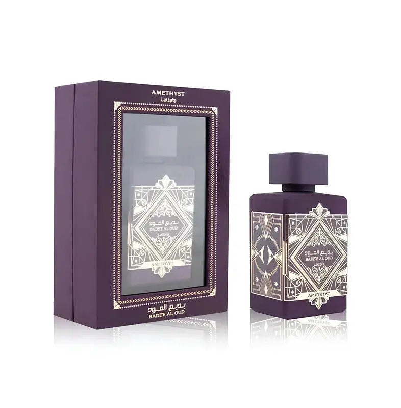 The image displays the packaging and perfume bottle of "Bade'e Al Oud Amethyst" by Lattafa. The perfume box has a deep purple color with a window on the front that showcases the perfume bottle inside, which features a similar design as the box. The packaging design includes intricate golden patterns and details that frame the window and the name of the perfume, giving it a luxurious and elegant appearance.