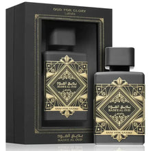  The image features a black perfume bottle with a matte finish, alongside its packaging. The bottle is labeled "BADE'E AL OUD" and "OUD FOR GLORY" by Lattafa. Both the bottle and the box bear intricate golden geometric and arabesque designs with the name written in both Arabic and English. The box has an open window through which the bottle is visible, framed by a golden border that matches the aesthetic of the bottle's design.