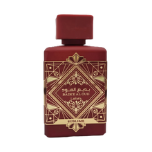 This image shows a deep burgundy perfume bottle with the name "BADEE AL OUD SUBLIME" from the brand Lattafa. The bottle has a matte finish with a matching square cap. It features a luxurious gold geometric pattern with traditional motifs, and the name is written in both Arabic and English. The word "SUBLIME" is displayed on a gold banner at the base. The design conveys a sense of rich heritage and sophistication.