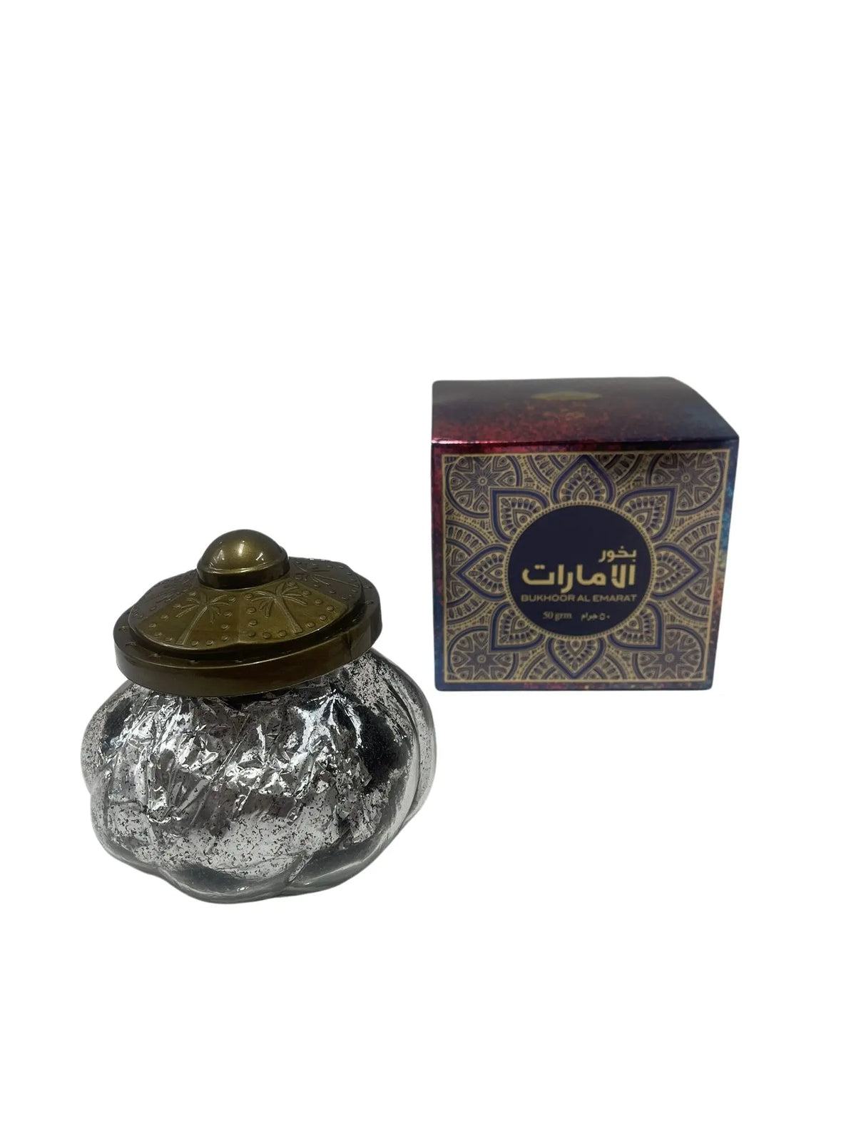 The image shows a product called "Bakhoor Al Emarat" by "Ard Al Zaafaran". It features an intricately patterned purple and gold box with Arabic script and English text. Next to the box is a decorative glass container with a silver foil texture and a brass-colored lid with embossed designs. The container seems to hold a traditional Middle Eastern scented product, typically used for burning and fragrance.