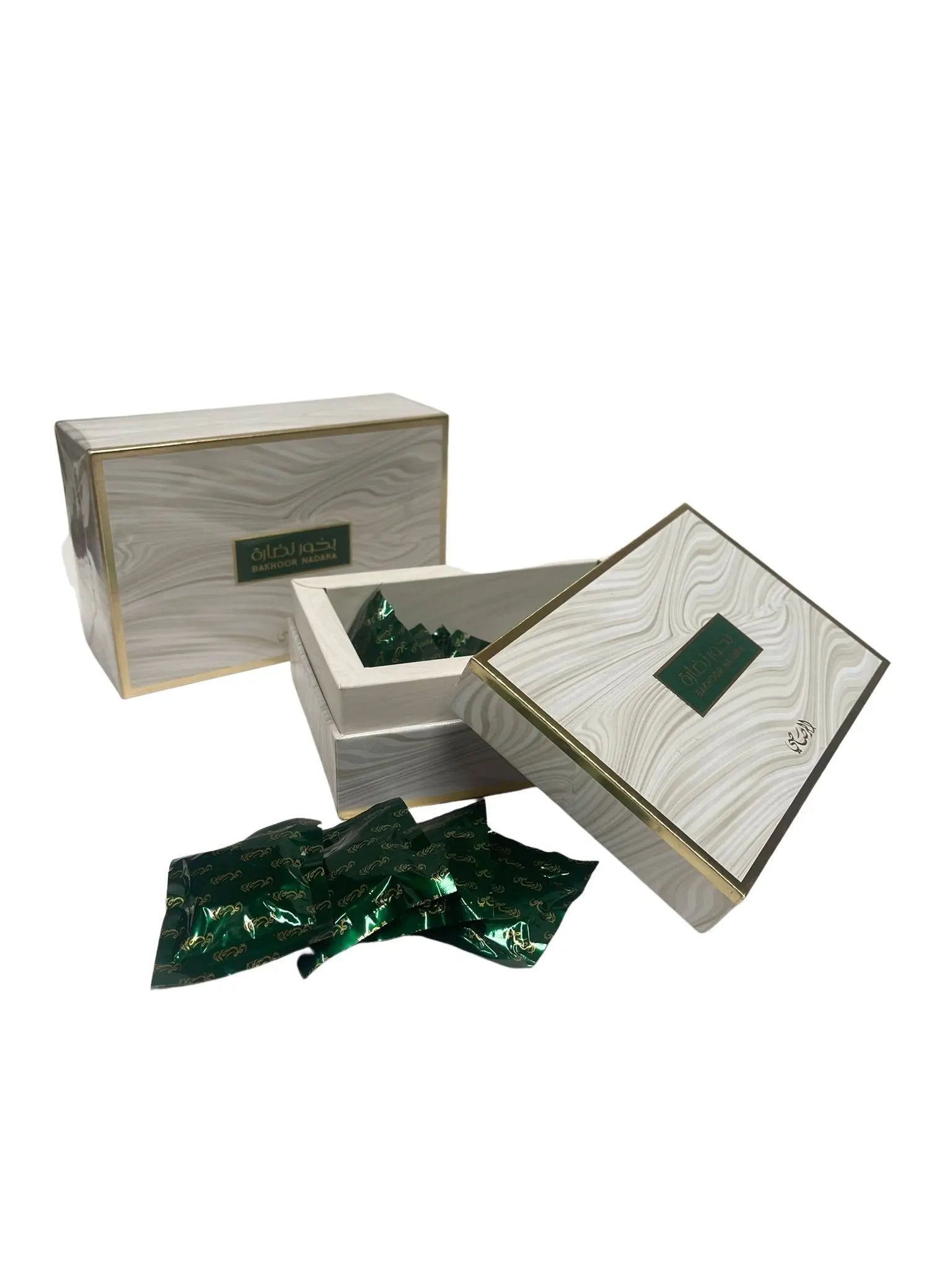 The image showcases a product named "Bakhoor Nadara" by "Al Rasasi". It includes a large wood-textured box with golden trimmings and a smaller, similarly designed open box revealing individual green sachets with Arabic script on them. These sachets are likely to contain the bakhoor - scented bricks or chips which are burned to perfume the home. The packaging conveys an air of exclusivity and tradition, emphasized by the use of classic colors and script.