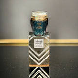 The image shows a product named "Bint Hooran Hand and Body Lotion." The lotion comes in a dark teal container with a clear lid and is placed on top of a matching box adorned with elegant geometric patterns and Arabic calligraphy. The box prominently features the product name "Bint Hooran" along with intricate designs in silver and gold. The luxurious and sophisticated packaging suggests a high-quality skincare product.